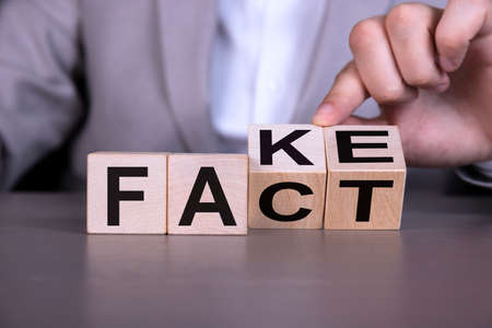 A businessman's hand turns over wooden cubes to change the wording from fake to fact.の写真素材