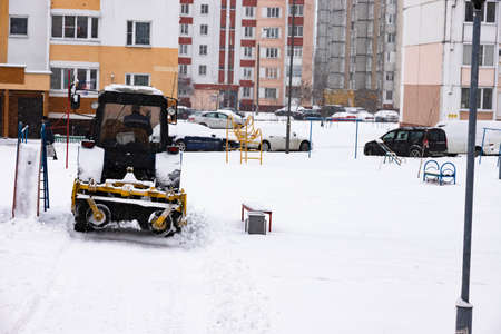 The tractor clears the road from snow in winter during a snowfall.の写真素材