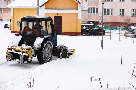 The tractor clears the road from snow in winter during a snowfall.の写真素材