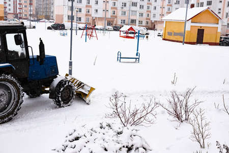 The tractor clears the road from snow in winter during a snowfall.の写真素材