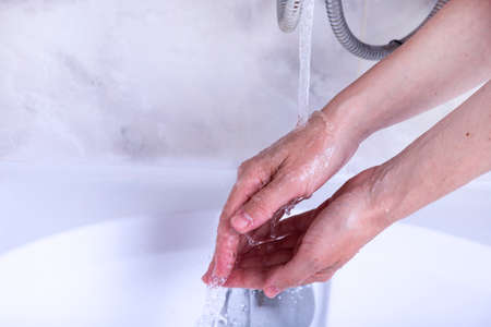 Hand washing process. Female hands under the tap with water in the bathroom.の写真素材