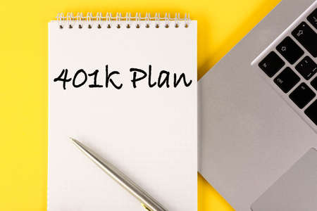 Paper with a 401k plan on the table with a laptop on a yellow background.の写真素材