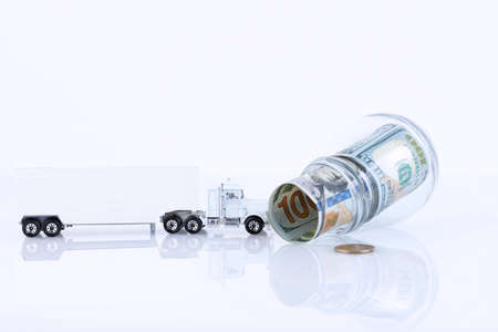 Glass jar full of 100 dollar bills lying sideways and a lorry isolated on white. Copy space.の写真素材