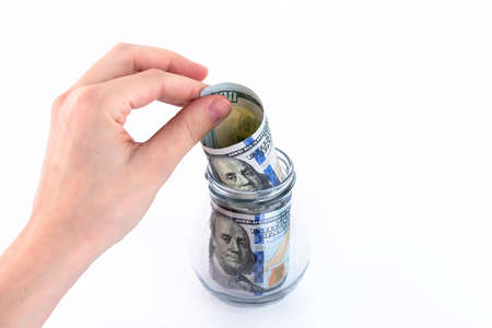 Hand folds paper American one hundred dollar bills, money in a glass jar. Concept for making...