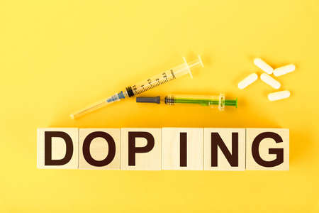 Doping, the text is written on wooden cubes on a yellow background and medical syringes.の写真素材