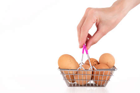 A female hand holds beige, wild chicken eggs in a shopper's basket on a white background. Selective focus. Copy space.の写真素材