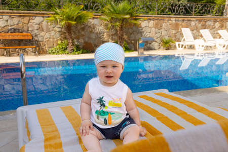 A handsome, little boy sits on a sun lounger by the pool. Selective focus.の写真素材