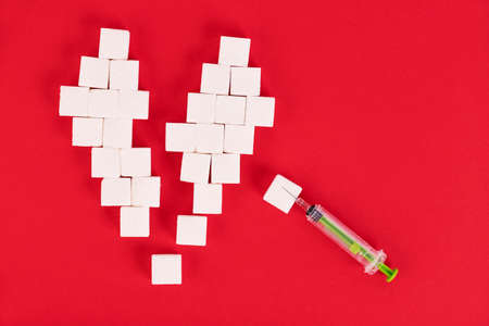 Broken heart made from sugar cubes and a syringe on a red background. Diabetes concept. View from above. Create space.の写真素材