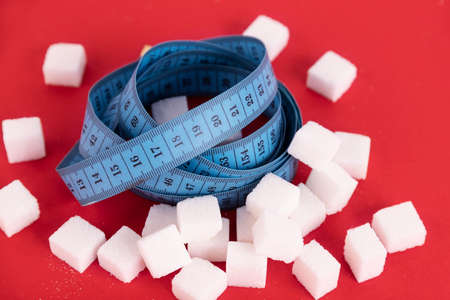 Diet without sugar for weight loss. A pile of white sugar cubes and a blue measuring tape in it. Red background. Copy space.の写真素材