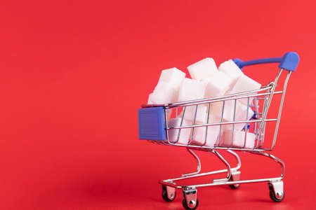 A shopper's cart is filled with refined sugar cubes on a red background. Copy space.の写真素材