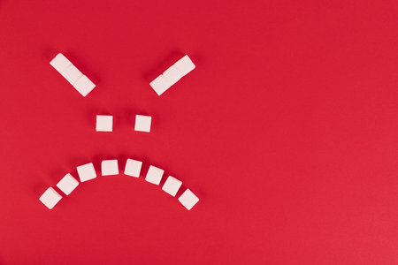 On a red background, cubes of white sugar, in the form of an evil emoticon. Copy space.の写真素材