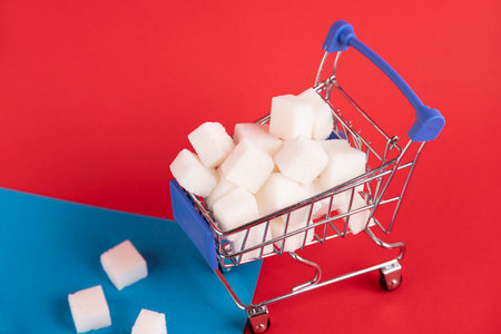 A shopper's cart is filled with refined sugar cubes on a red background. Copy space.の写真素材