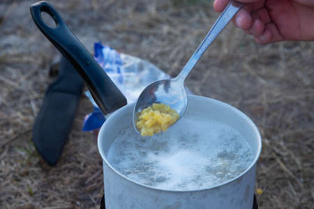 Pasta in a spoon and boiling water in a saucepan, tourist food in nature.の写真素材