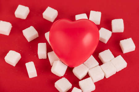 Broken heart made from sugar cubes and a syringe on a red background. Diabetes concept. View from above. Create space.の写真素材