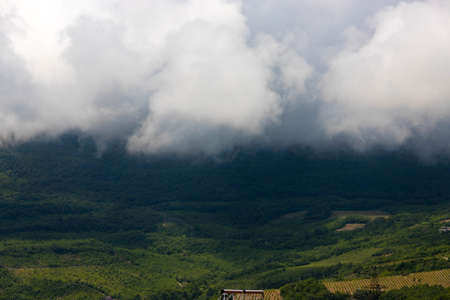 Rain clouds over mountains and a valley with a green vineyard.