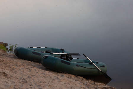 Two rubber boats with fishing tackle in the early morning during the fog, parked on the banks of the river.の写真素材