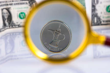 UAE currency dirham coin, view through a magnifying glass against the background of American dollars. Copy space.の写真素材