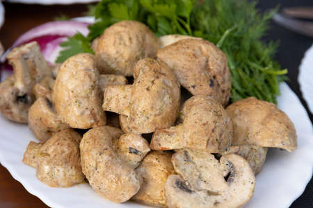 Grilled champignon mushrooms, lying on a white plate, decorated with herbs and red onions. Selective focus.の写真素材