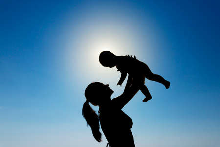 A young girl holds a child in her arms against the sun. Silhouette photography. High quality photoの写真素材
