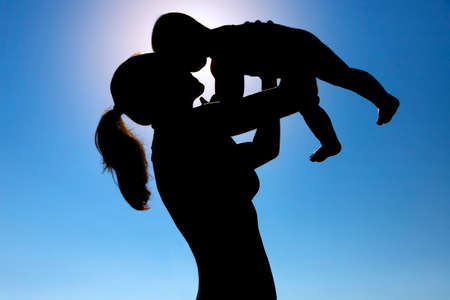 A young girl holds a child in her arms against the sun. Silhouette photography. High quality photoの写真素材