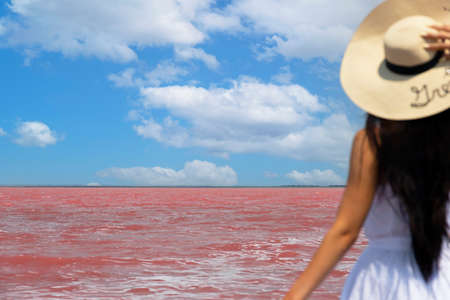 Woman traveler in hat looks at amazing exotic pink salt lake and blue sky. wanderlust travel concept, copy space for text. Selective focus. High quality photoの写真素材