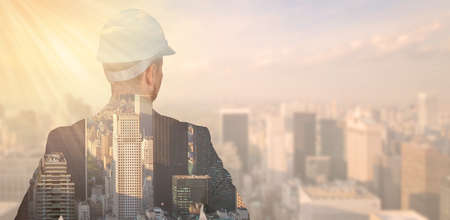 Double exposure of an engineer in a protective helmet against the background of the city, metropolis. High quality photoの写真素材