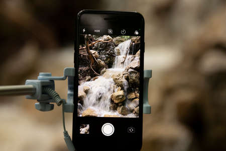 Taking pictures using a smartphone with a selfie stick on a blurred beautiful background. Close-up.の写真素材