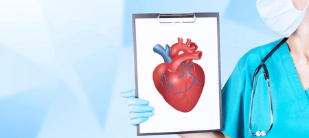 The hand of a cardiologist in medical clothes and a stethoscope holds a tablet with a realistic, voluminous, red heart on a light background. Cardiology concept. Copy space. High quality photoの写真素材