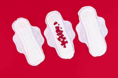 Many small red hearts, symbol of the menstrual cycle, on a feminine sanitary napkin. Feminine hygiene products during the menstrual cycle. Red background. Copy space. High quality photoの写真素材