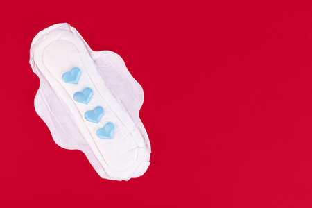 Four blue hearts as a symbol of the menstrual cycle on a feminine sanitary napkin. Feminine hygiene products during the menstrual cycle. Red background. Copy space. High quality photoの写真素材