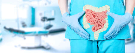 Close-up of a female surgeon doctor in a medical uniform and an icon of the intestine with a large intestine on the background of the operating table in the hospital, soft blurred background. high quality photoの写真素材