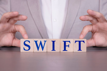 SWIFT, Businessman building a word from wooden cubes. The concept of financial regulation sanctions.の写真素材