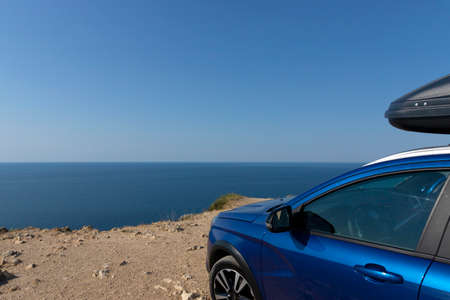 A blue car with a roof rack on the edge of a cliff against the blue sky and the sea. car travel concept. high quality photoの写真素材