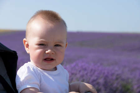 Close-up of a cute seven month old baby with blond hair smiling against the backdrop of a lavender...