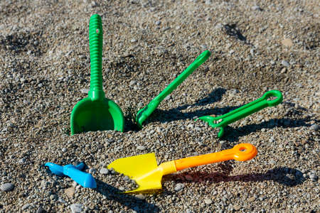 Children's toys on the seashore, multi-colored scoops, shovels and rakes lie on a rocky beach. child safety concept.の写真素材