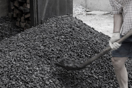 A worker with a shovel unloads black coal against the background of a large pile of coal. energy crisis. soft focus.の写真素材