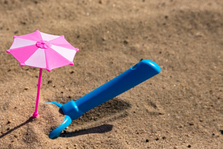 Children's sandbox, a toy pink umbrella and a blue shovel on a sandy beach. vacation with children. Children's psychedelicの写真素材