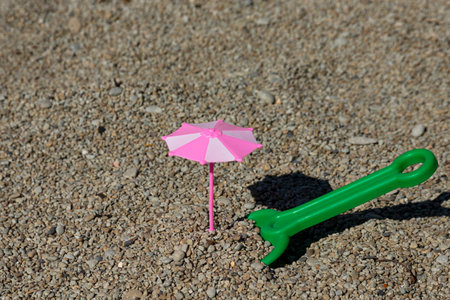Toy pink umbrella and baby green shovel on the beach. vacation with children.の写真素材