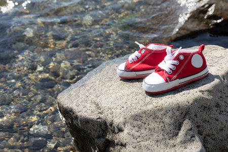 A pair of children's red sneakers stand on a rock by the sea.の写真素材