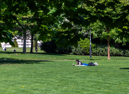 Young girl reading a book on a green lawn in a historical park. Austria, Viennaの写真素材
