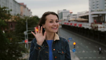 Cheerful, happy, smiling girl standing on the bridge, sends kisses, have fun, looks at the camera. Wind blows long dark hair beautiful young women. 4Kの写真素材