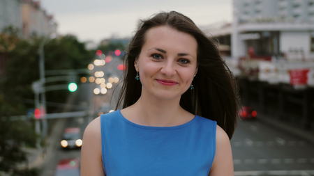 Wind blows long dark hair beautiful young women. happy, smiling girl in colorful blue dress standing on the bridge and looks at the camera. 4Kの写真素材