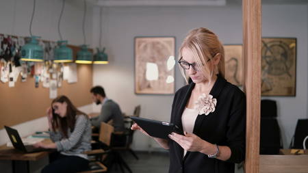 4k. beautiful blonde businesswoman uses a touchscreen tablet in the modern startup office.