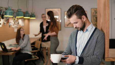 young handsome bearded man uses touchscreen tablet and drinking coffee in the modern startup office team in the workplaceの写真素材