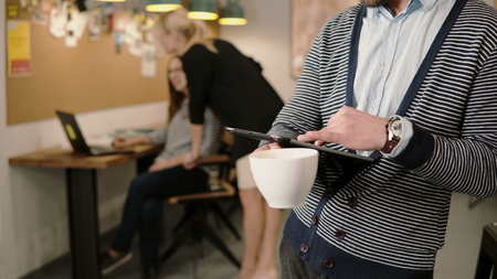 close-up of hands young man uses touchscreen tablet and drinking coffee in the modern startup office team in the workplaceの写真素材