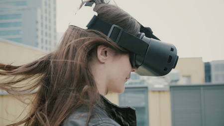 Brunette woman uses a virtual reality glasses on the roof. 4kの写真素材