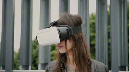 Brunette woman uses virtual reality glasses in the urban space. 4kの写真素材
