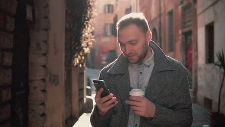 Portrait of Handsome man standing in the little street and using touchscreen technology at smartphone.の写真素材