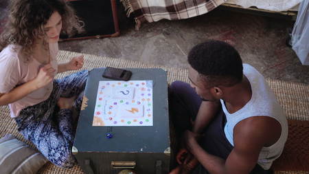 Multiracial couple, man and woman in pajamas playing the board game. Girl throws dice and dancing,...