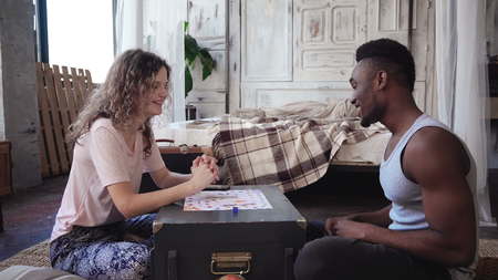 Man wins the board game and dance. Multiracial couple kiss and shake each other hands. Woman congratulates on a victory.の写真素材